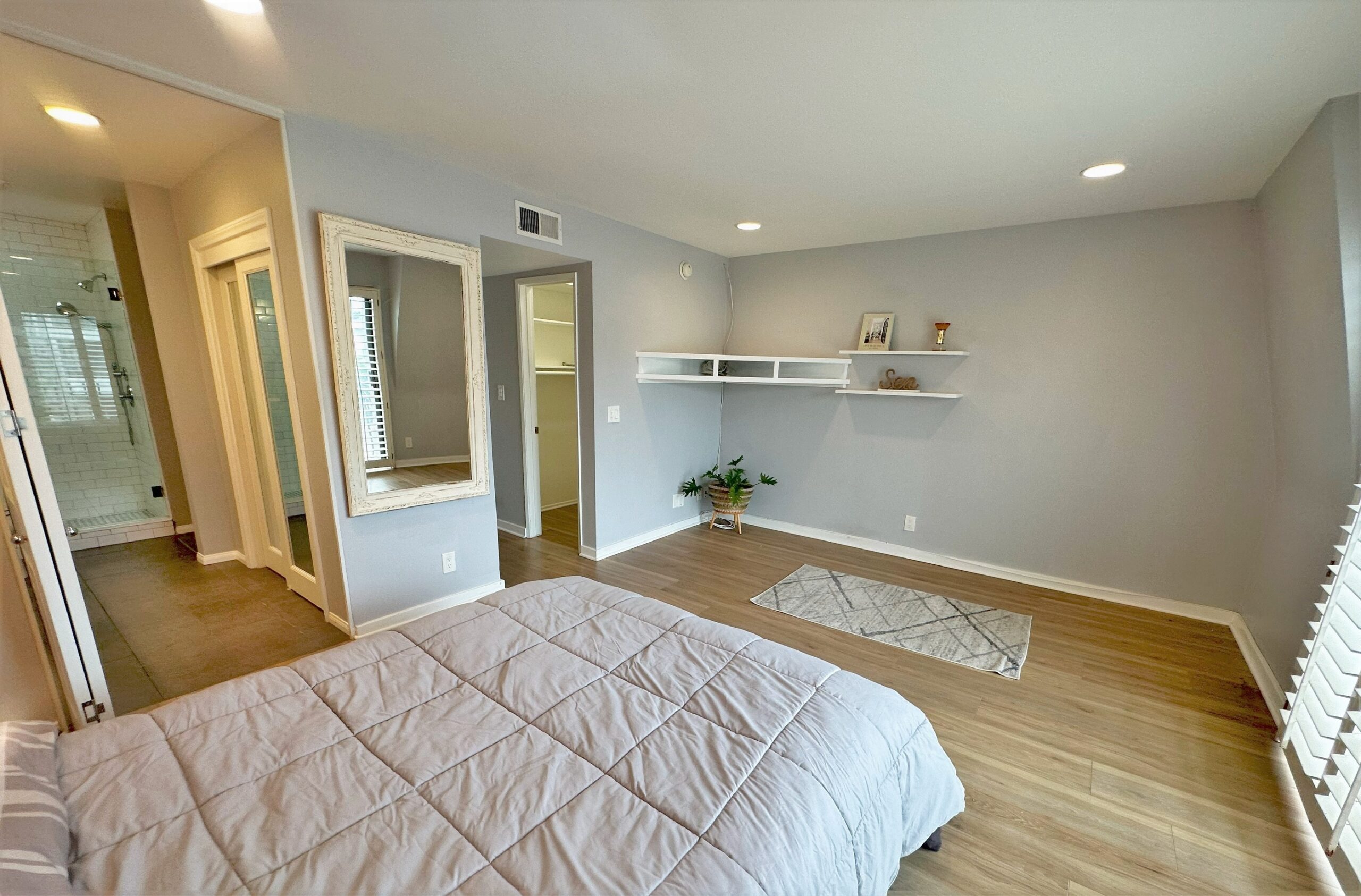 A bedroom with a bed, mirror and shelves.