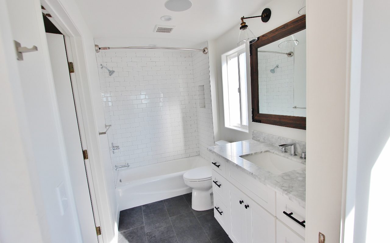 A bathroom with white cabinets and a toilet, sink, mirror, tub and shower.