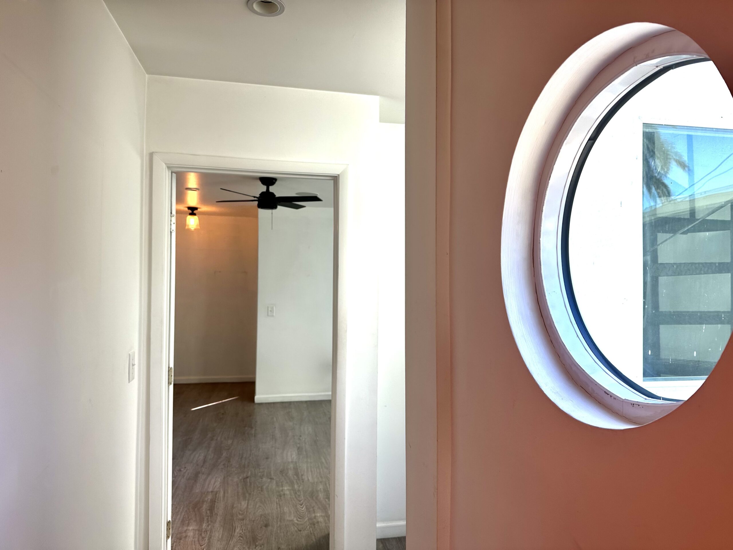 A hallway with a ceiling fan and a round mirror.