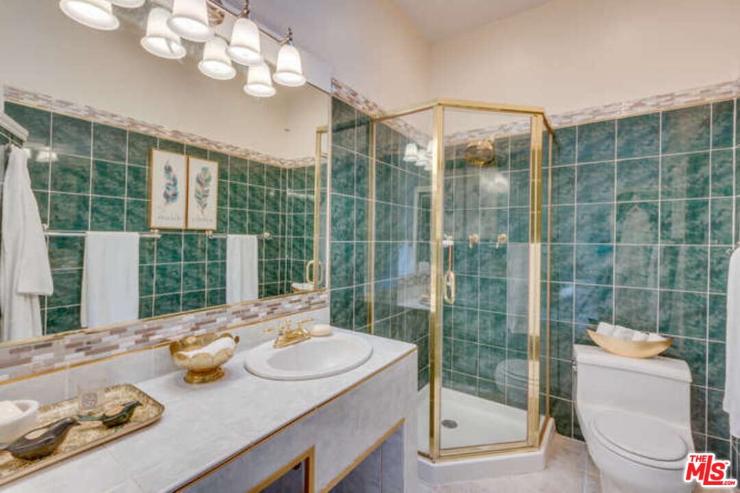 A bathroom with green tile and gold fixtures.